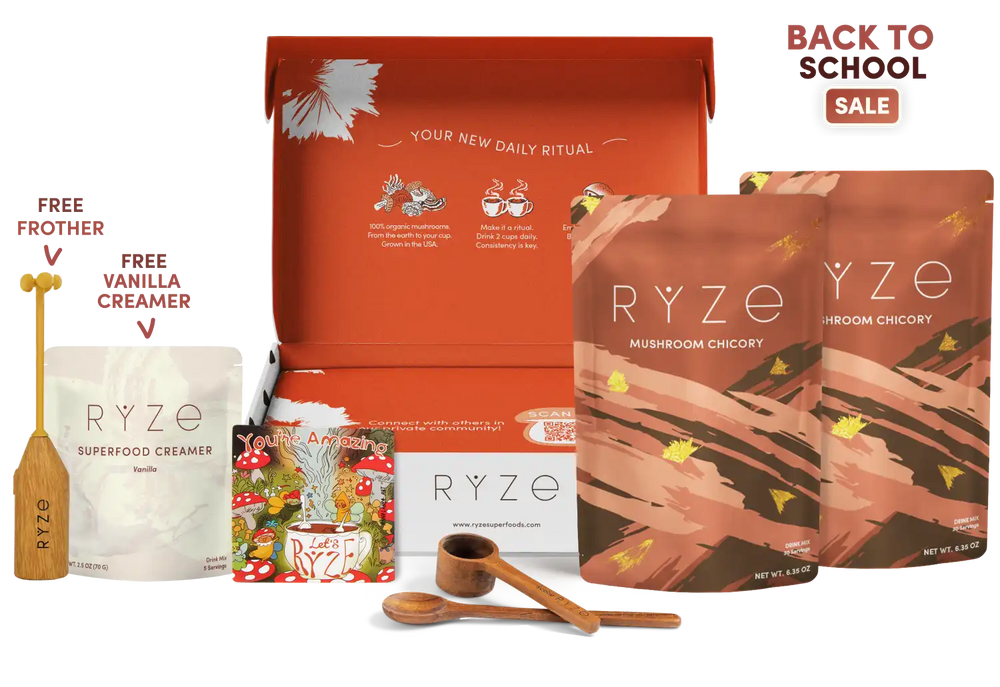A RYZE wellness gift set displayed on a white background with promotional text. The set includes a large orange-red box, two brown mushroom chicory pouches, a white superfood creamer pouch, a small illustrated magnet, two wooden measuring spoons, and a wooden frother.