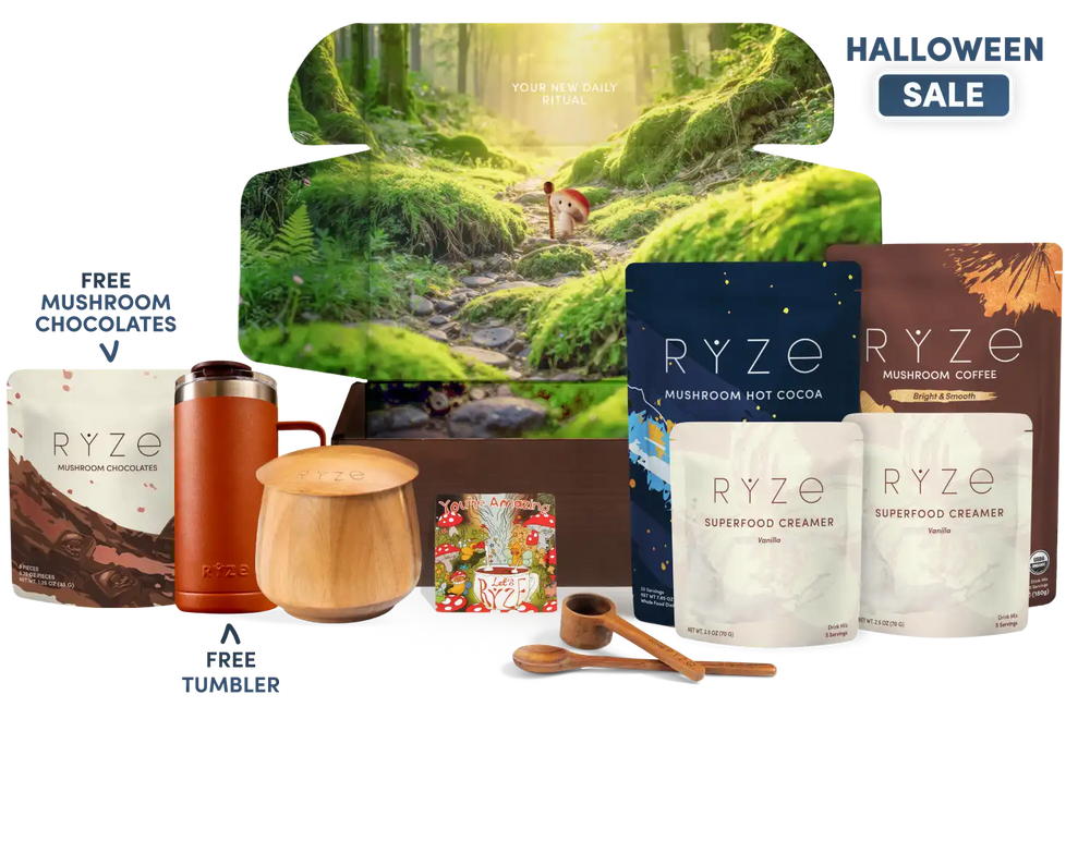 A curated coffee gift set arranged on a white background with a large illustrated forest box behind it. Visible products include multiple RYZE mushroom coffee pouches, a brown insulated tumbler, a wooden mug with lid, wooden spoon and scoop, and a small floral box.