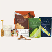 Collection of RYZE products including Mushroom Coffee, Hot Cocoa, Matcha, Superfood Creamer, a magnet, a wooden frother and spoons on a white background